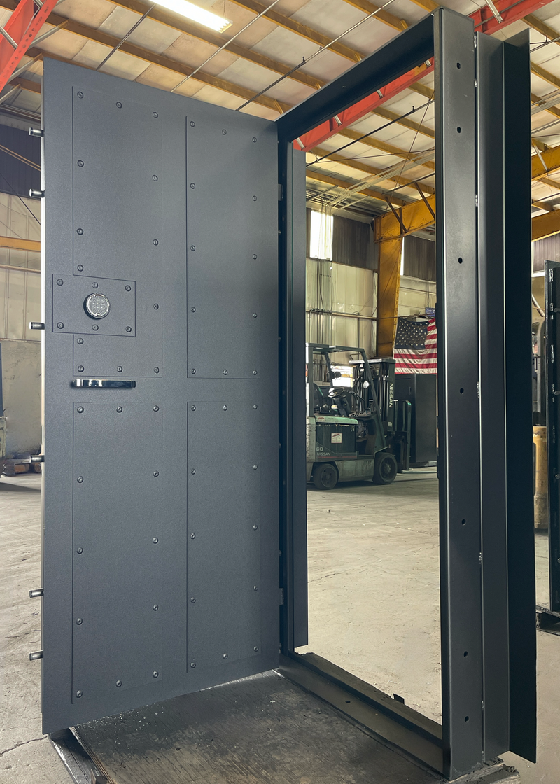 Large metal vault door in a warehouse setting with forklifts in the background