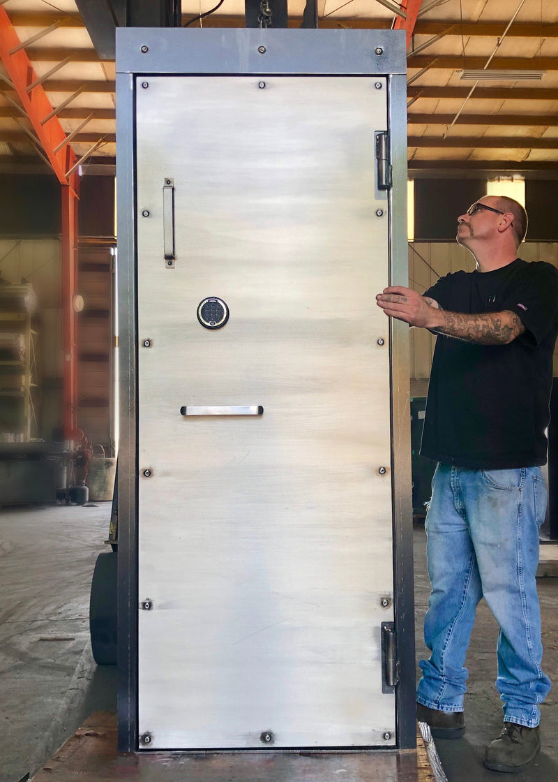 Person standing next to a large metal vault door on a forklift in an industrial setting